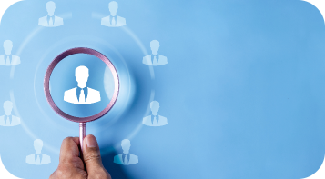 A hand holding a magnifying glass focuses on a person icon among several identical icons on a blue background, symbolizing targeted selection or recruitment.